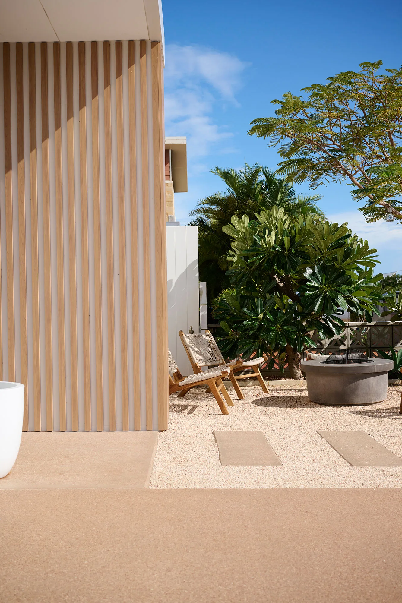 Exmouth I home — outdoor courtyard with timber batten wall, woven loungers and frangipani